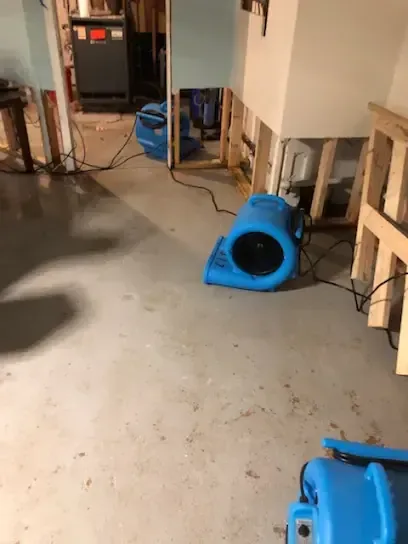 An air mover drying a basement floor where the lower drywall was cut away