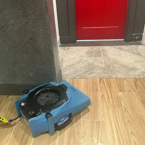 An air mover running on a wood-look tile floor near an open doorway during drying