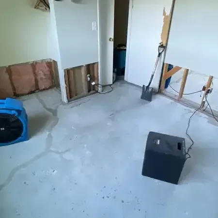 Air movers and a dehumidifier running on a bare floor after the lower drywall was removed