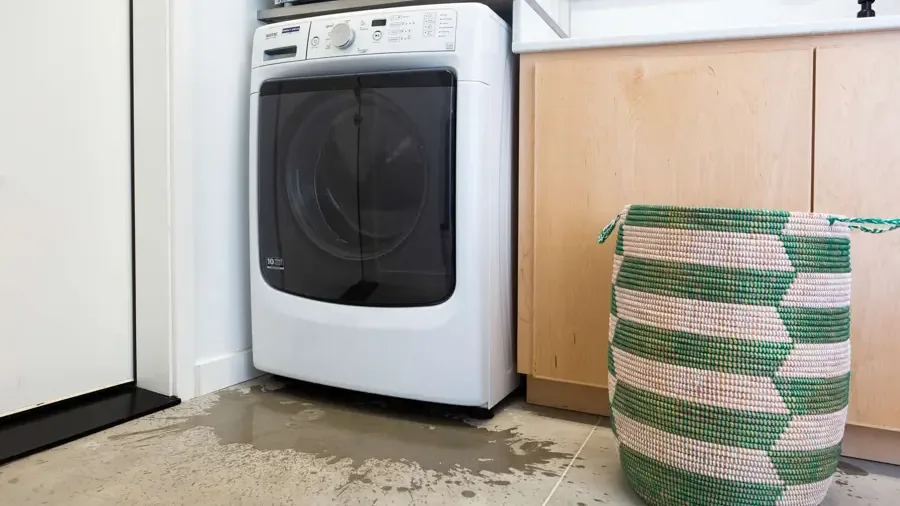 Water running out from under a washing machine across a laundry floor