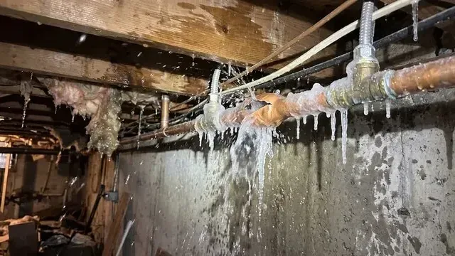 Icicles hanging from frozen pipes along a foundation wall under a house