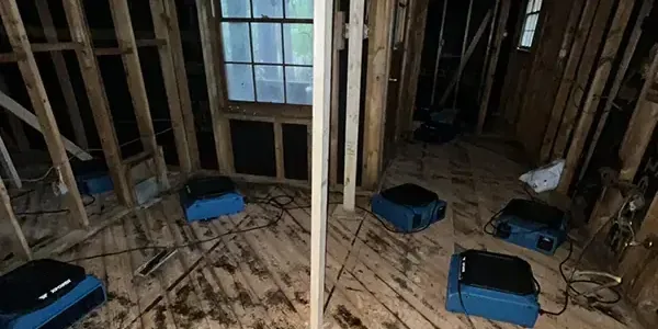Air movers blowing across a subfloor and opened wall framing during structural drying
